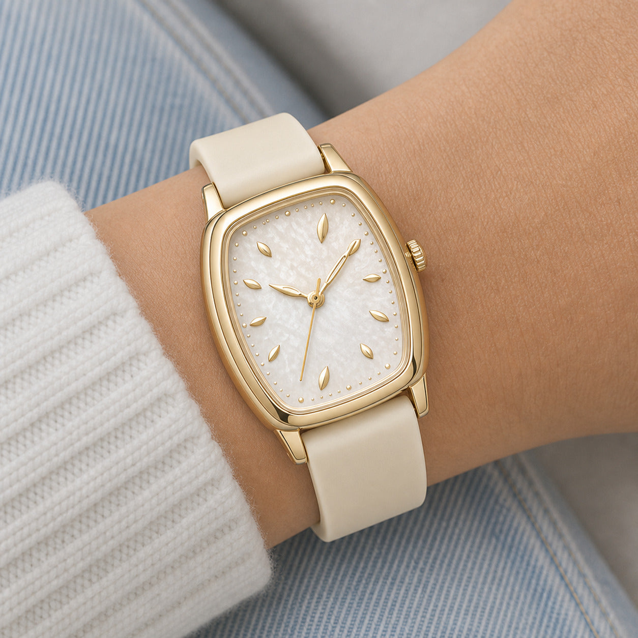 Gold watch with beige strap on a wrist against a light background