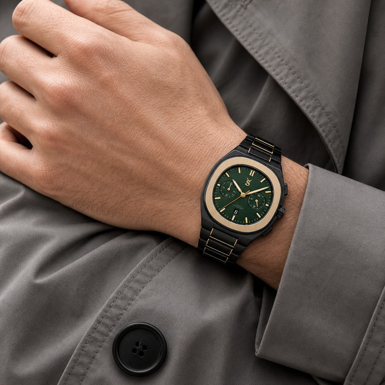 Hand wearing a green wristwatch with a detailed face, against a gray coat background