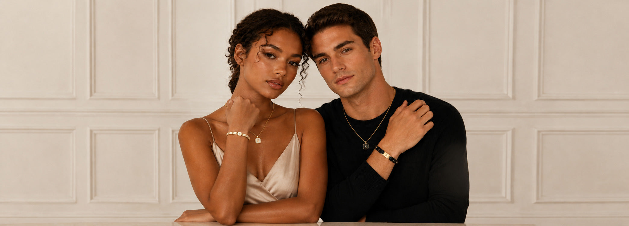 Two people sitting together against a light-colored paneled wall.