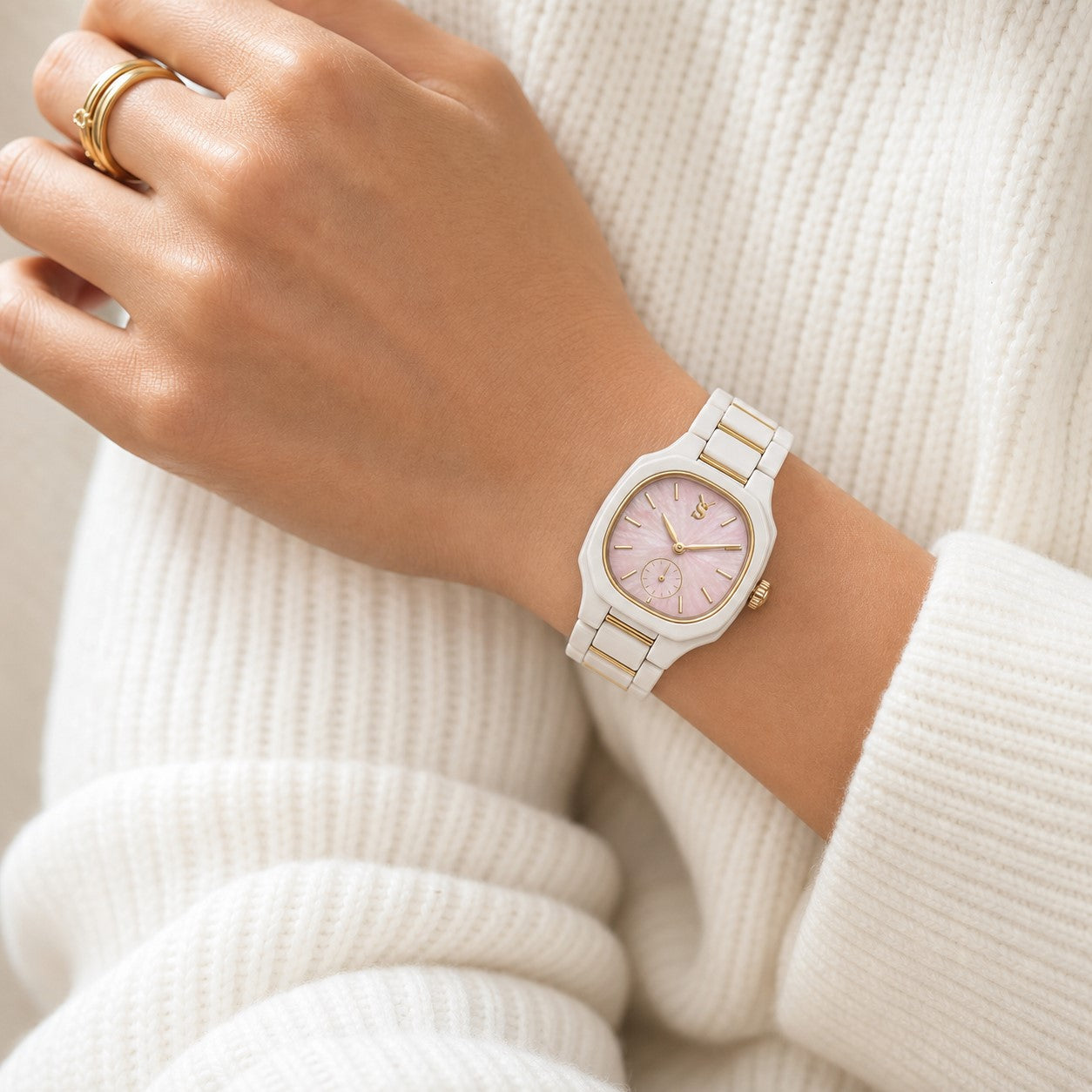Hand wearing a light-colored watch with a pink face on a white background