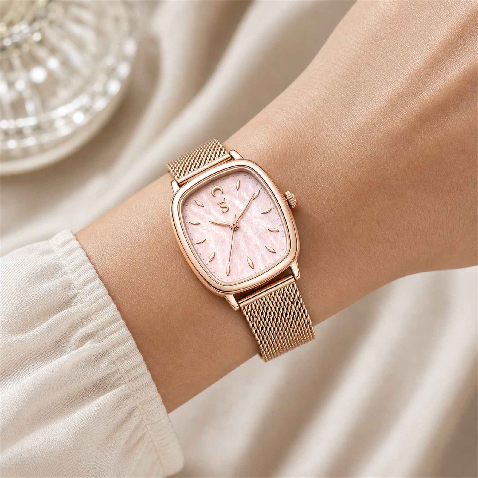 Rose gold watch with a pink face on a wrist against a neutral background