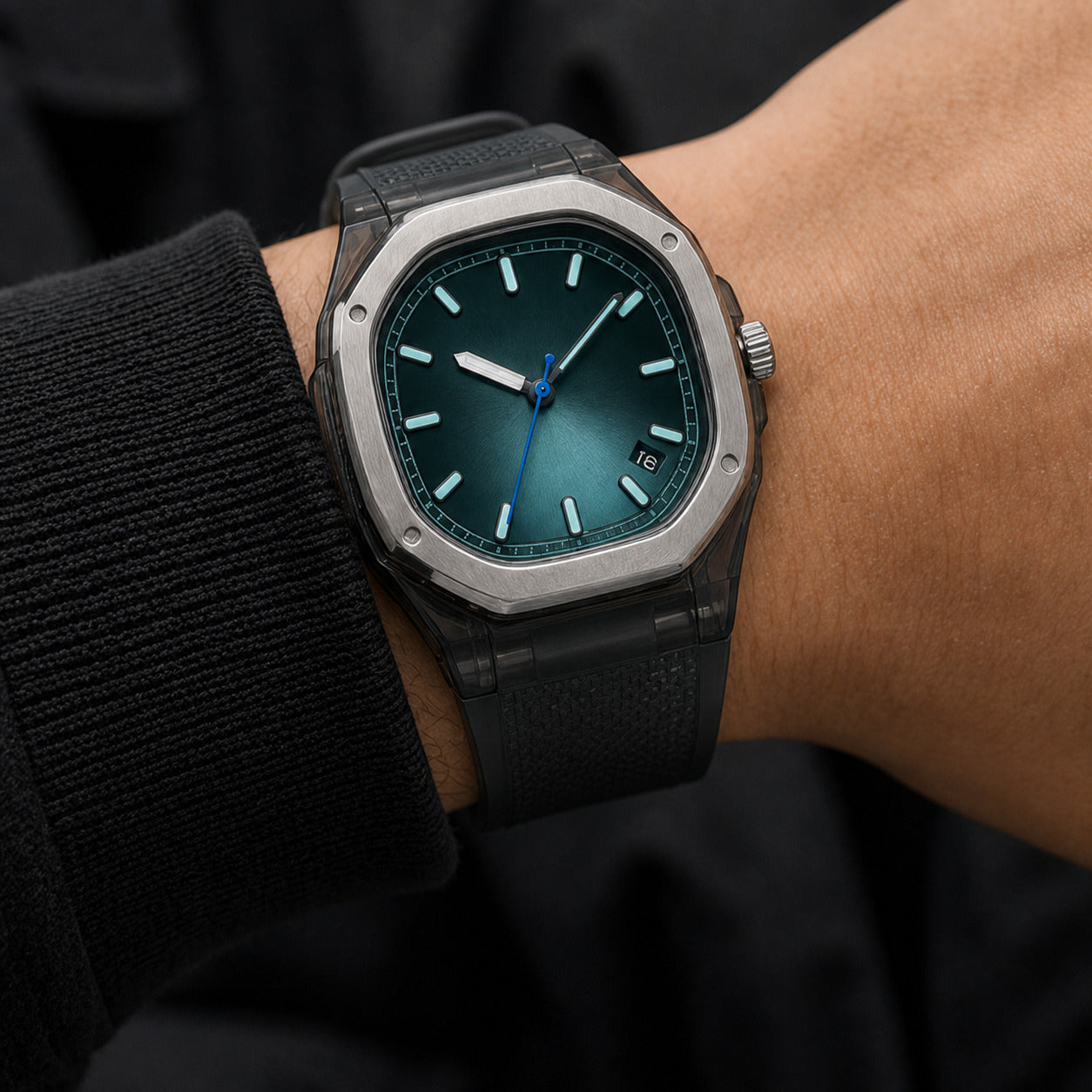 Watch with a dark green face and black strap on a wrist against a dark background