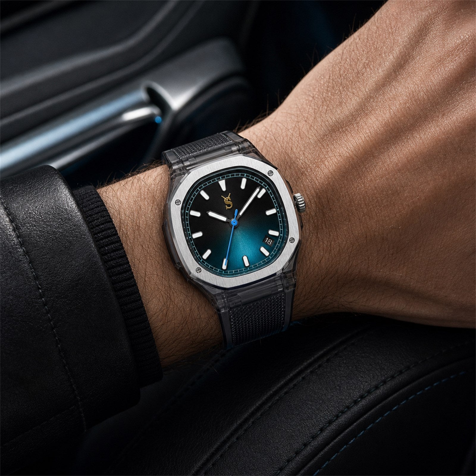 Black wristwatch with blue dial on a person's wrist, sitting inside a car.